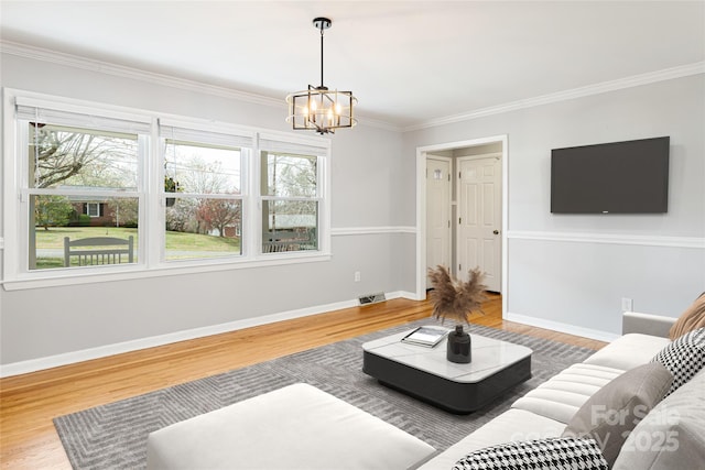 living room with plenty of natural light, wood finished floors, ornamental molding, and an inviting chandelier