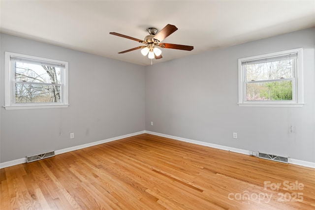 spare room featuring light wood finished floors, baseboards, visible vents, and a ceiling fan