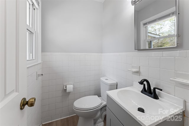 half bathroom with wood finished floors, vanity, tile walls, toilet, and wainscoting