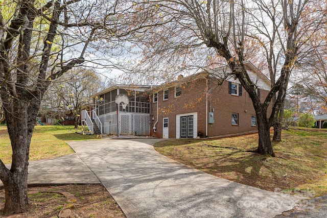 view of front of home with a front yard, brick siding, a sunroom, and driveway
