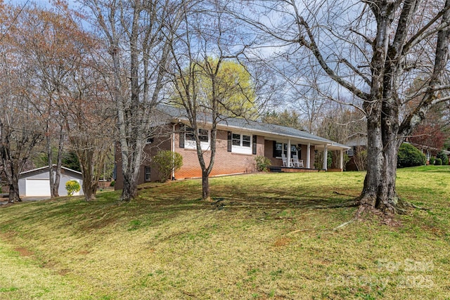 single story home featuring a front yard, covered porch, an outbuilding, brick siding, and a garage