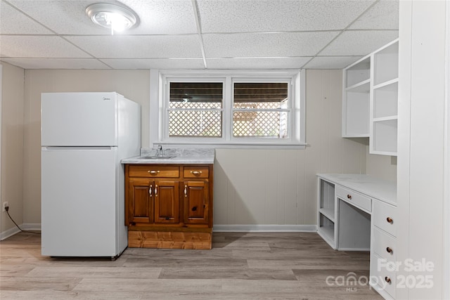 kitchen featuring light wood finished floors, open shelves, brown cabinetry, and freestanding refrigerator