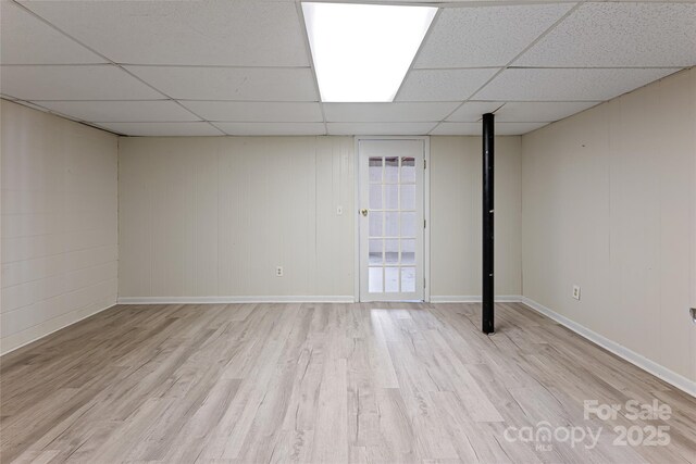 finished below grade area with baseboards, wood finished floors, and a drop ceiling