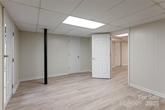 finished basement featuring a paneled ceiling, baseboards, and light wood-type flooring