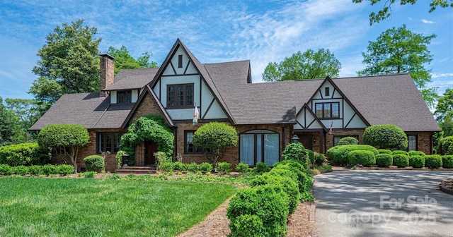 418 3rd St NE, Hickory, NC 28601 - tudor home featuring a front lawn, a chimney, brick siding, and roof with shingles