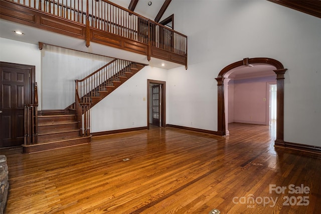 418 3rd St NE, Hickory, NC 28601 - unfurnished living room featuring arched walkways, decorative columns, a towering ceiling, wood finished floors, and stairs