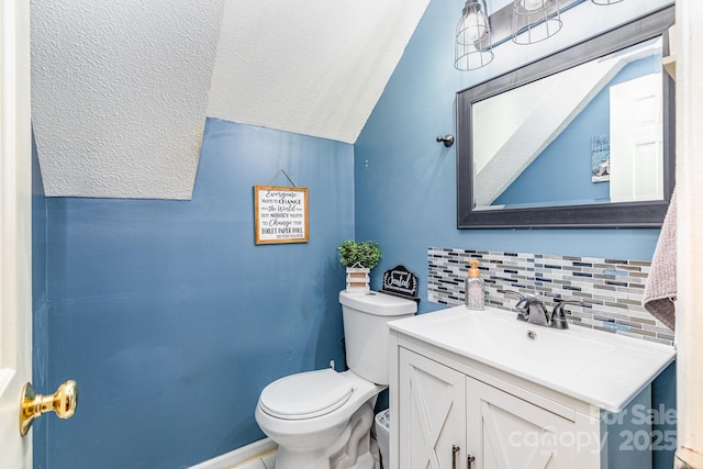 bathroom with backsplash, a textured ceiling, vaulted ceiling, vanity, and toilet