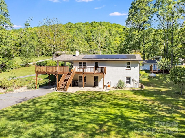 back of property with a wooden deck, a patio area, stairway, a forest view, and solar panels