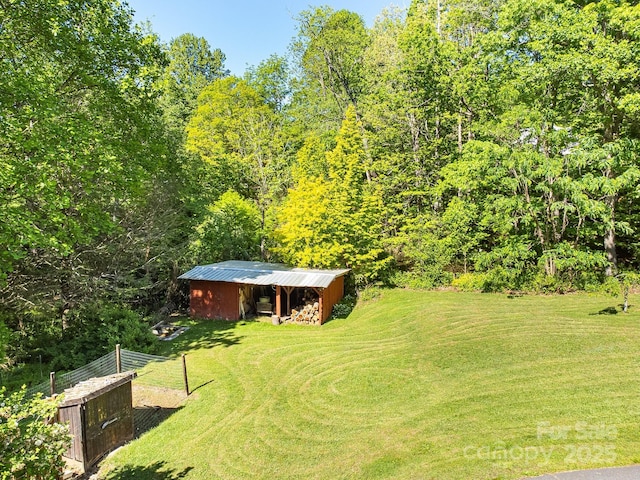 view of green lawn featuring a pole building, an outdoor structure, and a view of trees