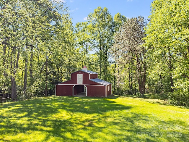 view of green lawn with a barn, an outbuilding, a garage, and a view of trees