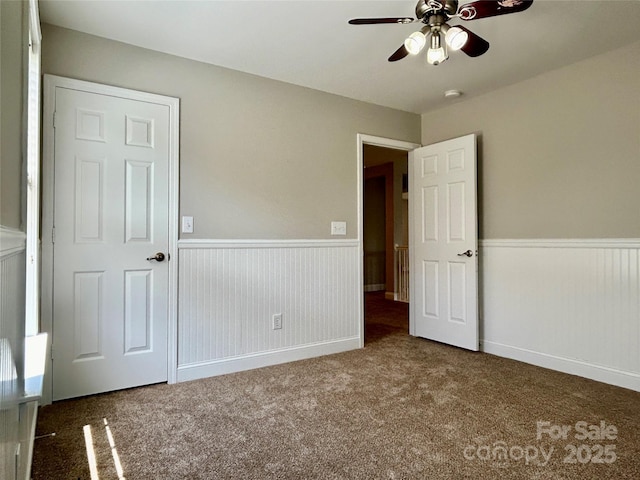 unfurnished bedroom featuring wainscoting, ceiling fan, and carpet