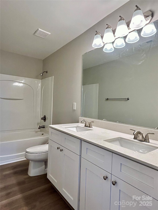 full bath with a sink, double vanity, toilet, and wood finished floors