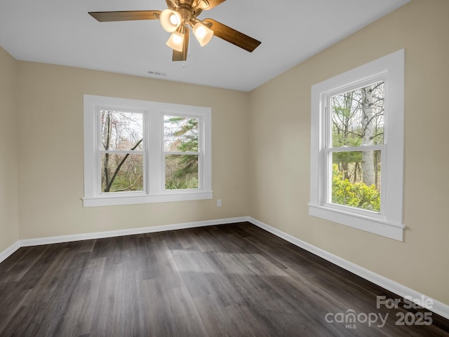 empty room with baseboards, dark wood-style flooring, visible vents, and a ceiling fan