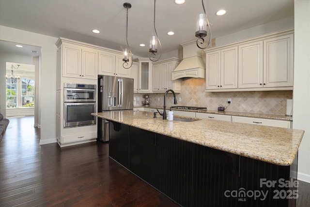 kitchen with light stone countertops, dark wood finished floors, appliances with stainless steel finishes, a sink, and custom range hood