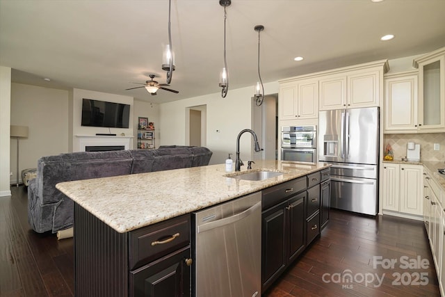 kitchen with a sink, tasteful backsplash, appliances with stainless steel finishes, dark wood finished floors, and a center island with sink