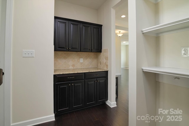 kitchen with dark wood-style floors, dark cabinetry, baseboards, and backsplash