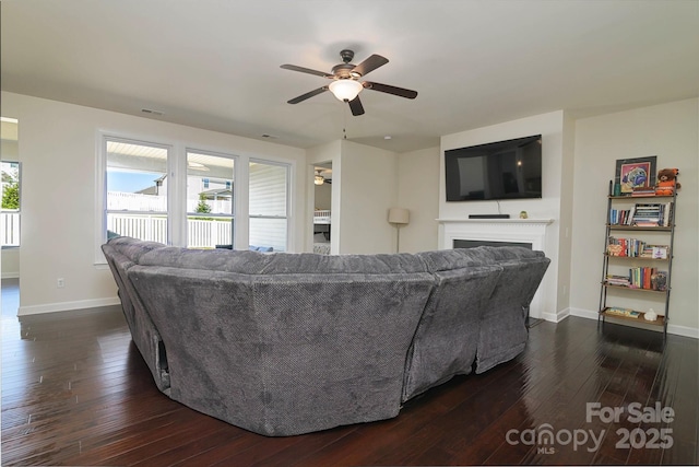 living area with a ceiling fan, dark wood-type flooring, a healthy amount of sunlight, and a fireplace