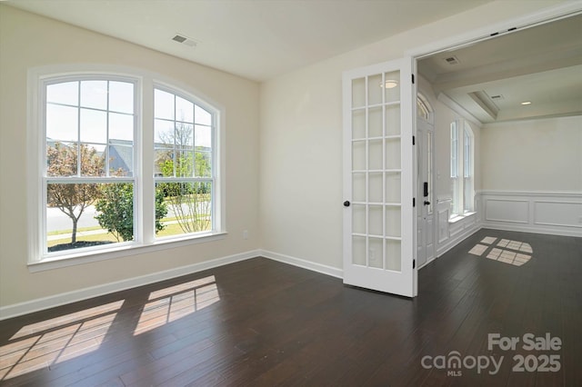 unfurnished room featuring dark wood-style flooring, baseboards, a wainscoted wall, visible vents, and a decorative wall