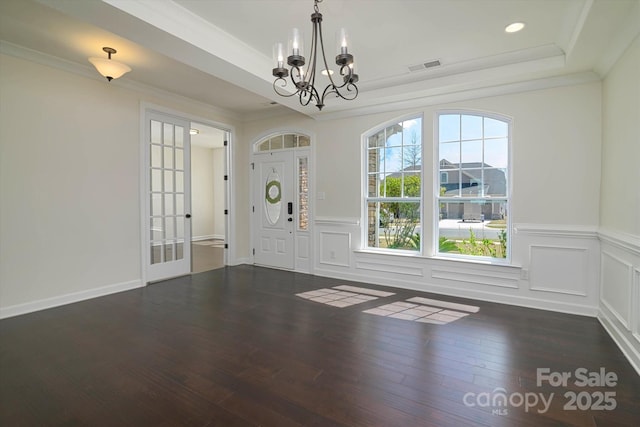 entrance foyer featuring a tray ceiling, a notable chandelier, crown molding, dark wood-style floors, and visible vents