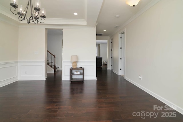 interior space featuring stairway, an inviting chandelier, a decorative wall, ornamental molding, and dark wood-style flooring