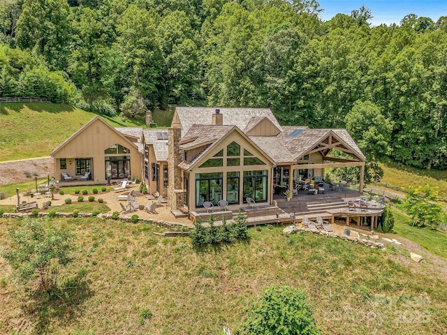 back of property with a lawn, a deck, a view of trees, and a chimney