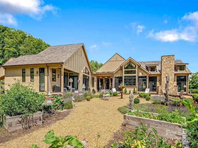 back of property with board and batten siding, a chimney, and a vegetable garden