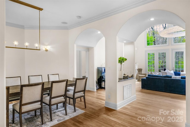 dining area with arched walkways, baseboards, visible vents, light wood-style floors, and ornamental molding