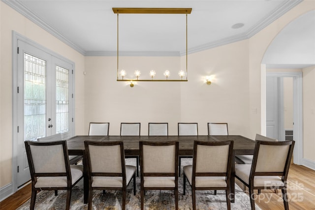 dining space with arched walkways, crown molding, and wood finished floors