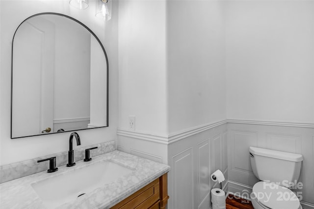 bathroom featuring a wainscoted wall, a decorative wall, toilet, and vanity