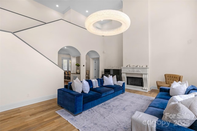 living area featuring baseboards, a towering ceiling, arched walkways, a fireplace, and wood finished floors