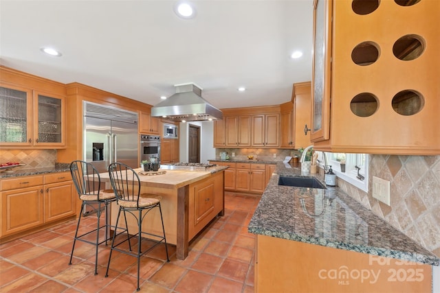 kitchen with tasteful backsplash, built in appliances, a sink, wooden counters, and island range hood