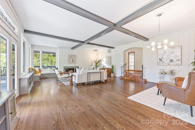 living area with arched walkways, a warm lit fireplace, beam ceiling, and wood finished floors