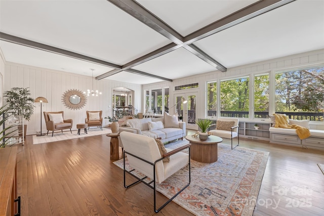 living area with beam ceiling, plenty of natural light, an inviting chandelier, and hardwood / wood-style flooring