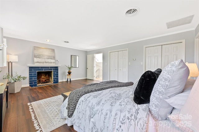 bedroom with dark wood-type flooring, crown molding, visible vents, and multiple closets