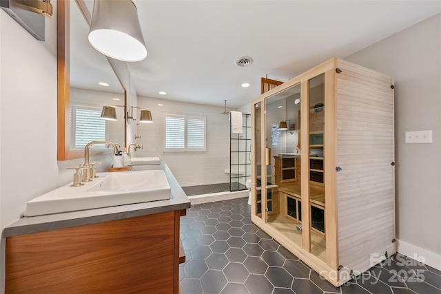 full bath featuring a walk in shower, tile patterned flooring, double vanity, and a sink
