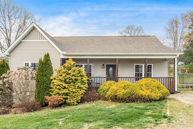 view of front facade featuring a trampoline, a front yard, a porch, and a shingled roof