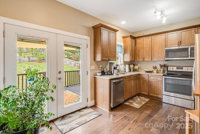 kitchen with dark wood-style flooring, stainless steel appliances, a sink, light stone countertops, and brown cabinets