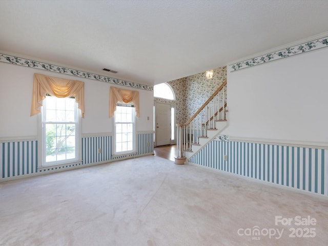 unfurnished living room with wallpapered walls, carpet flooring, visible vents, and a wainscoted wall