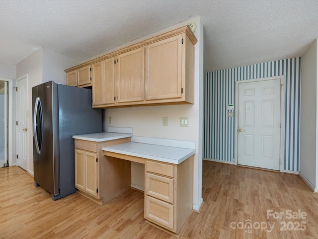 kitchen with light countertops, built in desk, freestanding refrigerator, and light brown cabinetry