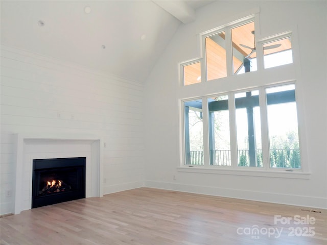 unfurnished living room with visible vents, light wood-type flooring, beam ceiling, a lit fireplace, and high vaulted ceiling