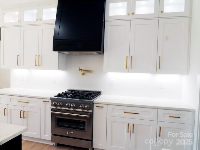 kitchen with light stone counters, stainless steel stove, exhaust hood, and white cabinetry