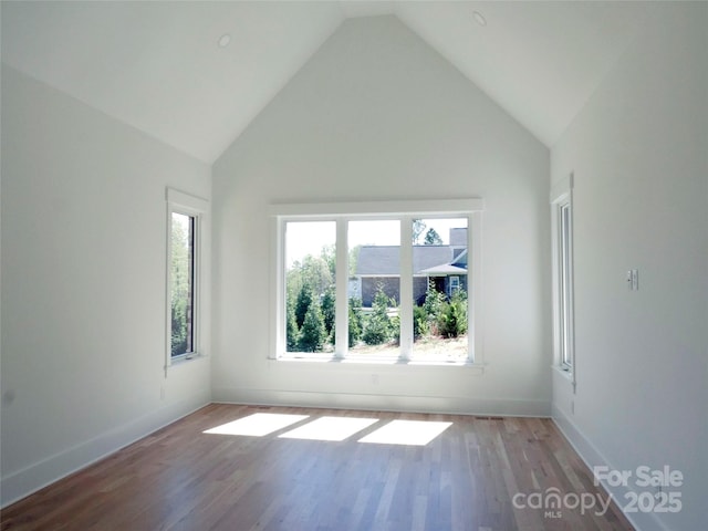 spare room with baseboards, vaulted ceiling, and wood finished floors
