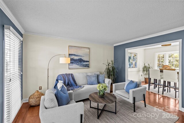 living area with a textured ceiling, baseboards, ornamental molding, and wood finished floors