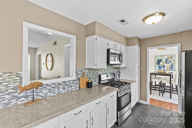 kitchen with white cabinetry, decorative backsplash, appliances with stainless steel finishes, and visible vents