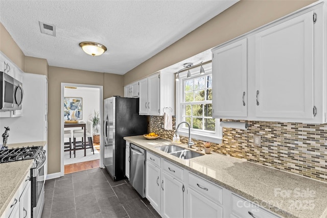 kitchen featuring visible vents, stainless steel appliances, white cabinetry, a sink, and backsplash