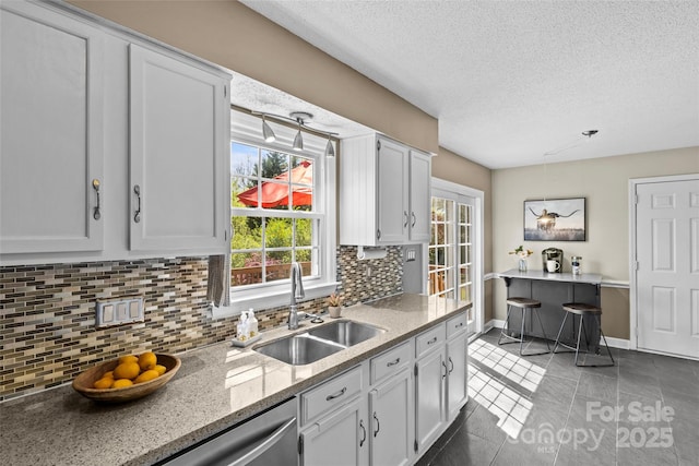 kitchen featuring decorative backsplash, a textured ceiling, dishwasher, white cabinetry, and a sink