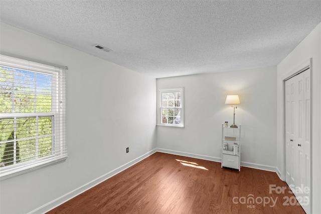 unfurnished bedroom with dark wood-type flooring, baseboards, a textured ceiling, visible vents, and a closet