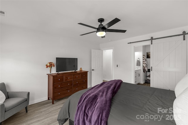 bedroom featuring a ceiling fan, a barn door, light wood-type flooring, baseboards, and visible vents