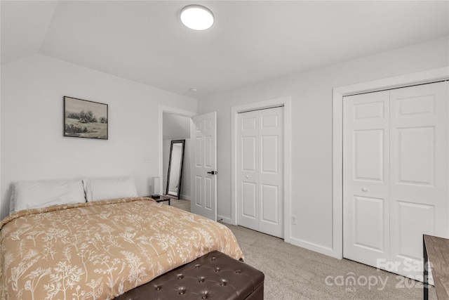bedroom featuring baseboards, lofted ceiling, two closets, and carpet