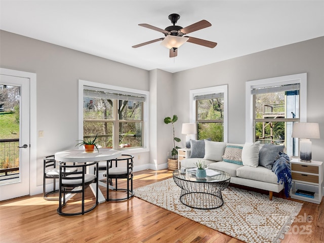 living area with baseboards, ceiling fan, and light wood-style floors